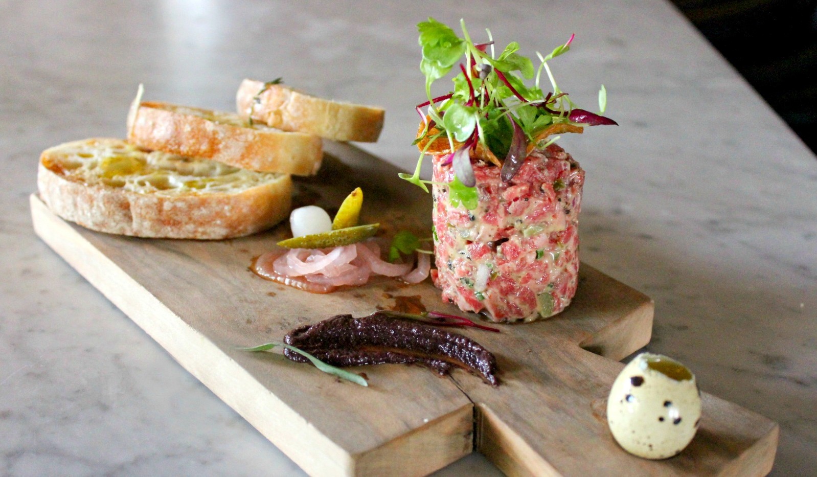 Steak tartare on cutting board with bread slices 